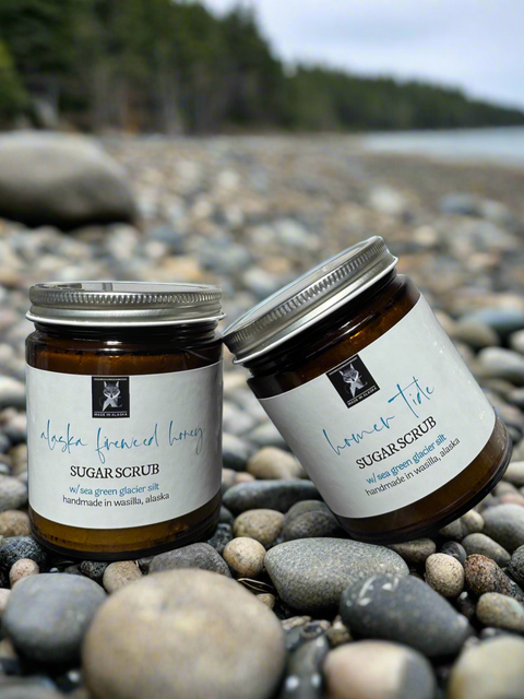Two jars of sugar scrub on pebbles with a blurred natural background