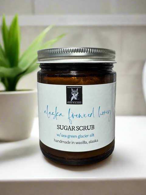Jar of Alaska Fireweed Honey sugar scrub on a bathroom counter with a plant in the background